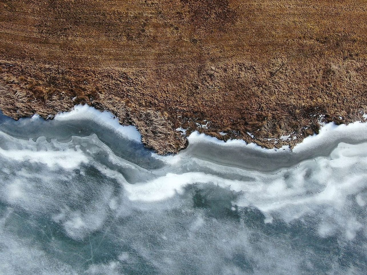 Água tranquila do lago sob o gelo abaixo de morros baixos
